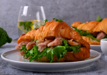 Croissant sandwich with pieces of hot smoked fish catfish clarias on grey table