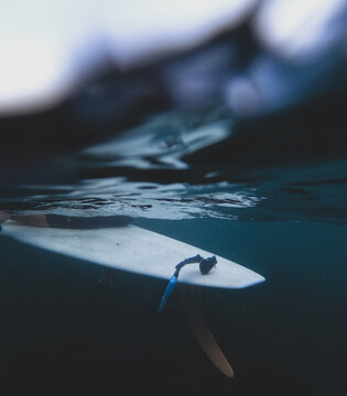 Surfboard tail and fin underwater split view with sky and ocean ripples