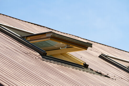Open roof window in brown metal sheet roofing under blue sky | Otwarte okno dachowe w brązowym blaszanym dachu na tle błekitnego nieba