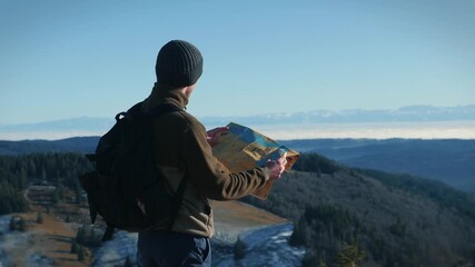 Man in sports outdoors clothes with backpack and map in hands at mountain top