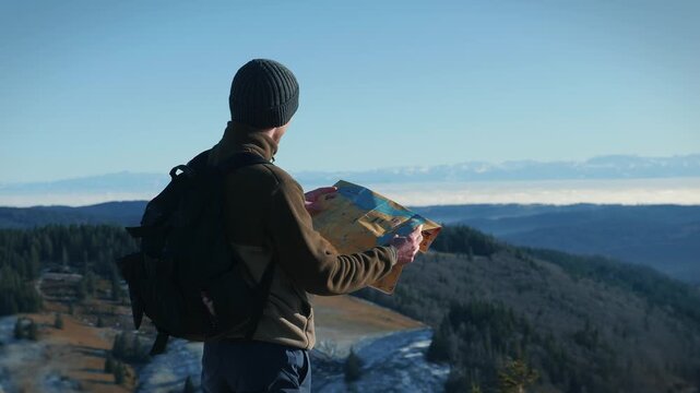 Man in sports outdoors clothes with backpack and map in hands at mountain top