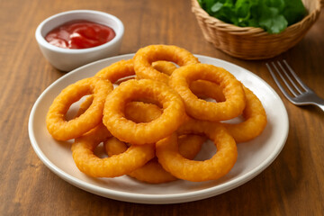 Crispy golden onion rings served on a white plate with ketchup dip, delicious deep-fried snack on wooden table