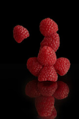 A tower of fresh raspberries on a black background with a reflection. A dramatic composition...