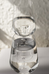 A glass of pure water and a carafe on a textured background with a play of light and shadows. A...