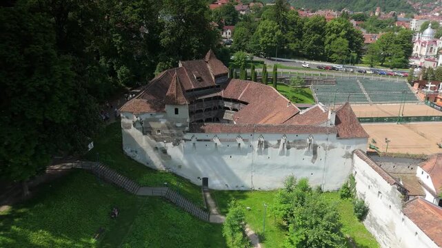 Aerial semicircular drone flight around Bastionul Tesatorilor in Brasov, revealing three fortified walls under Tampa hill with forest, Schei district and old town in summer morning light