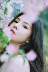 Close-up of a young woman amidst blooming flowers in a serene outdoor setting.