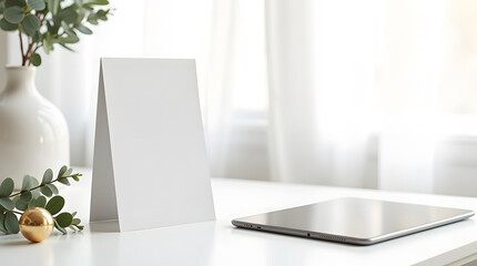 Blank white card mockup with vase, eucalyptus, and tablet on a bright white desk.