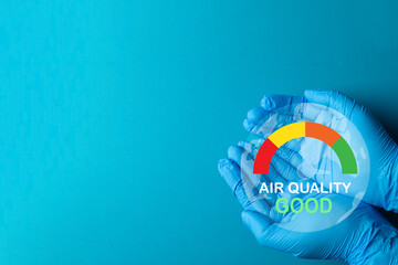 Hands in protective gloves hold a good Air Quality Index (AQI) icon. A concept for environmental protection, safety from pollution, and the goal of achieving clean air. Blue background.
