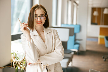 A stylish and confident professional woman is posing elegantly with a pen in a modern, contemporary...