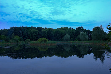 Calm summer evening, dusk after sunset on a forest lake. Harmonious widescreen panoramic side view...