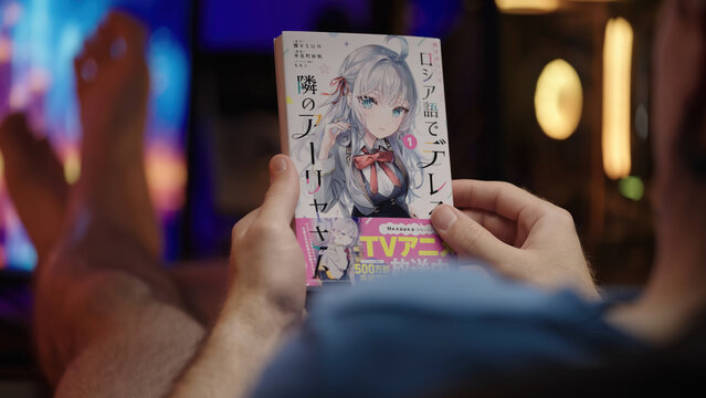 Reading Japanese manga Alya Sometimes Hides Her Feelings with pc in background, over shoulder view