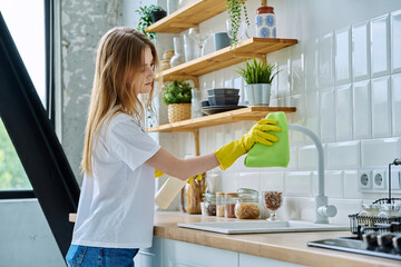 Young woman in rubber gloves cleaning kitchen, wiping dust with rag