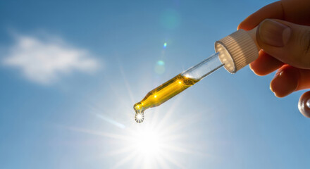 Dropper held in hand with golden liquid serum supplement sparkling in sunlight, essential oil, vitamin D, vitamin E, vitamin A, omega 3-6-9, retinol, jojoba oil, argan oil, hemp oil