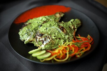 Pomfret fish served with green sauce on a black plate in a restaurant background