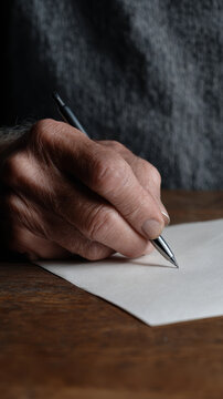 Elderly hand writing letter on paper with pen, thoughtful expression