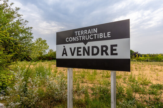 "Terrain constructible &agrave; vendre" &eacute;crit en Fran&ccedil;ais sur un panneau pos&eacute; sur un terrain vague sans construction. Concepts de vente et d'achat de terrains &agrave; construire et de march&eacute; immobilier en France