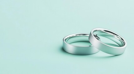 Matching platinum wedding bands with a flat profile and brushed texture, isolated on a pastel mint background