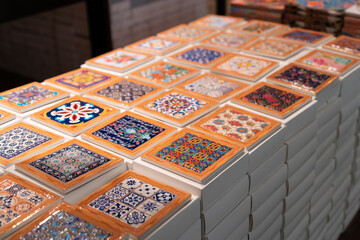 Decorative ceramic trivet with intricate patterns arranged neatly on white box stacks, showcasing vibrant colors and artistic designs in a market or retail environment.