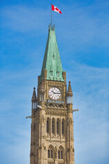 Obraz premium Ottawa, Ontario, Canada. May 20, 2024: The Peace Tower of Canada's Parliament buildings stands tall under a vibrant blue sky, its iconic clock and Canadian flag prominently displayed.
