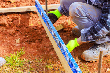 Construction worker uses level tool on wooden frame for proper alignment in yard preparation for...