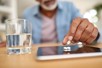 Older man takes medication at home while using a tablet and drinking water in the morning