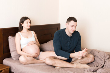 Happy pregnant family. Husband massaging his pregnant wife legs and sitting together on couch in...