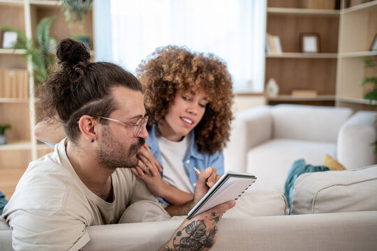 Young couple making plans writing on notebook at home - Powered by Adobe