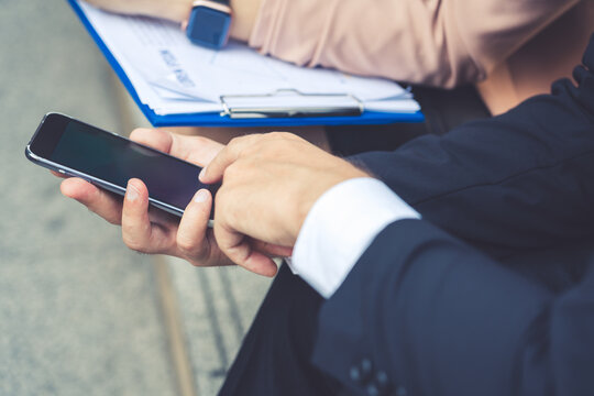 A close-up shot of a businessman using his smartphone, with a document folder in the background. represents the convenience of mobile technology and modern communication in the business world.