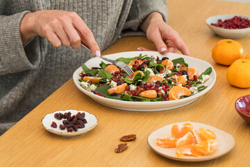  Woman eating winter salad with fresh spinach, mandarin and pomegranate at wooden table.