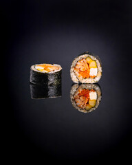 An elegant and minimalist studio shot of a cut Gimbap (or sushi) roll on a reflective black surface. The image features a single roll sliced into two pieces, showcasing the rich and colorful fillings 