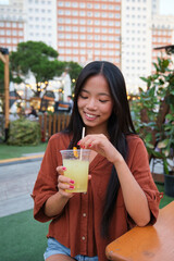 Happy young woman holding a refreshing drink at a summer festival, enjoying the lively atmosphere