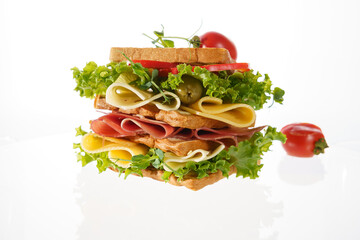 Delicious sandwich stacked high with fresh vegetables, meats, and cheeses on a white background