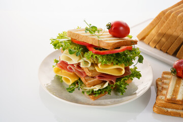 Delicious stack of fresh sandwich with layers of lettuce, meats, and cheeses on a white plate ready to be enjoyed