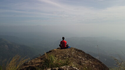 Freedom and adventure &mdash; man sitting on cliff edge overlooking majestic mountains and valley under blue sky