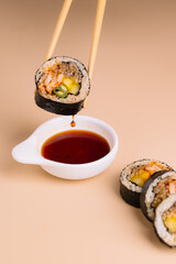 vertical shot of a piece of Gimbap (Korean seaweed rice roll) held by chopsticks and dripping soy...