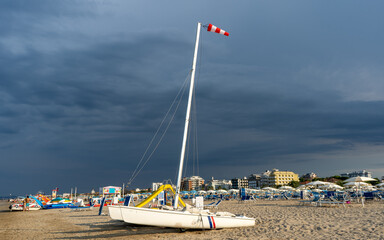 Windsock stormy sky over sandy beach in summer. Catamaran sun loungers and umbrellas. Empty coastline in summer wind