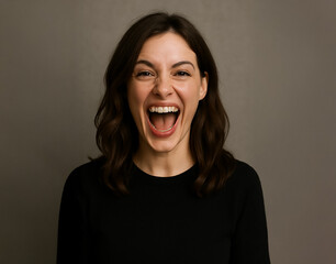 junge Frau mit schwarzen Haaren vor neutralem grauen Hintergrund, zeigt starke Begeisterung