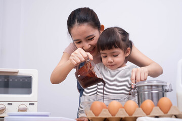 A joyful moment in the kitchen as a mother teaches her daughter how to cook, pouring chocolate into a mixing bowl filled with eggs.