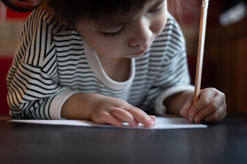 A focused child writes on paper, showcasing creativity and concentration in a cozy environment. kid doing homework ,education concept