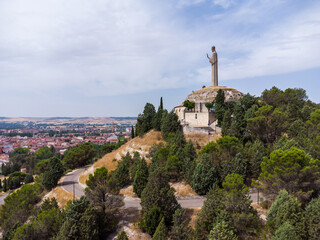 Side-view drone shot of the Cristo del Otero on one side of the scene and the city of Palencia on the other.