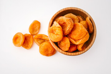 Wooden bowl filled with dried apricots on a clean white background, showcasing their vibrant orange...