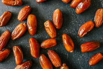 Close-up of dried dates scattered on a dark textured surface, showcasing their rich brown color,...