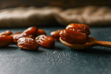 Scattered dried dates on a dark background with a wooden spoon. A healthy, naturally sweet snack full of energy and nutrients, often enjoyed during Ramadan and in Middle Eastern cuisine