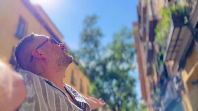 POV Point of view of male latin cheerful traveler tourist spreading arms wide, experiencing moment of pure joy during summer vacation in Madrid, feeling sense of freedom amid vibrant urban landscape.