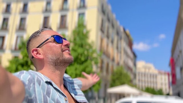 POV Point of view of male latin cheerful traveler tourist standing with open arms feeling joy while experiencing vibrant Madrid cityscape during summer vacation radiating freedom and happiness