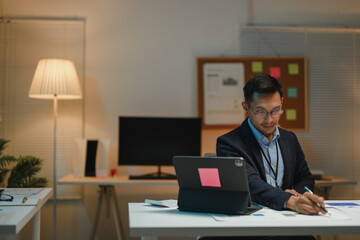 Asian businessman working late at night in office writing notes on documents