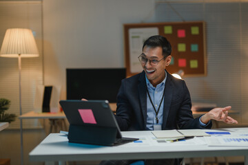 Asian businessman having video call and smiling during late night work in office