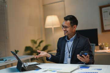 Asian businessman having video call and holding smartphone in office at night