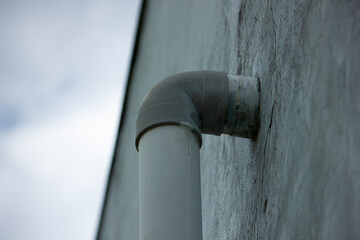 A grey PVC plastic pipe elbow emerging from a concrete wall against an overcast sky. Minimalist industrial and architectural concept