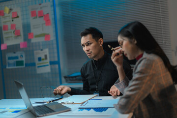 Business people working late and looking worried at laptop in office meeting room